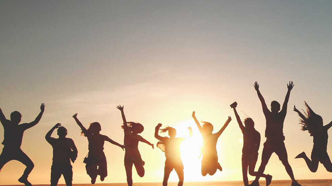 nio ungdomar hoppar. i bakgrunden syns en solnedgång