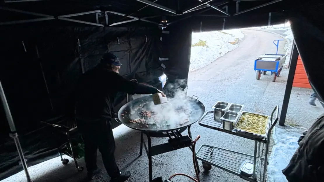 Person lagar mat på en stor stekpanna under ett tält.