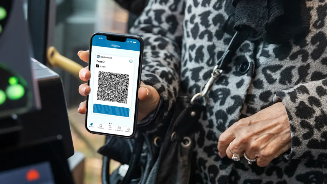 En senior håller i en mobiltelefon inne i en buss som visare QR.kod för en seniorbiljett.
