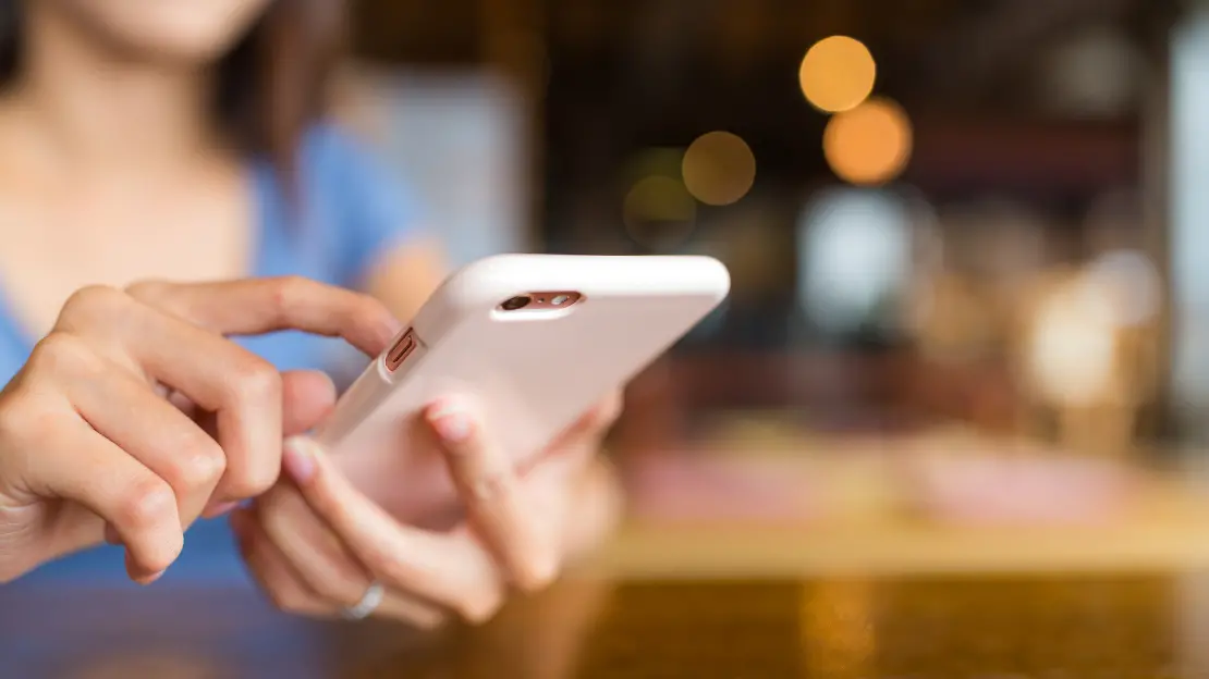 Två händer som håller i en rosa mobiltelefon och skriver i den.