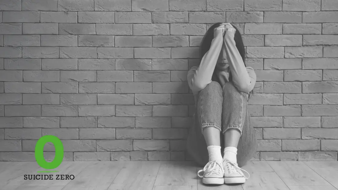 Person sitter på golvet med armarna framför ansiktet. I hörnet finns loggan för Suicide Zero.
