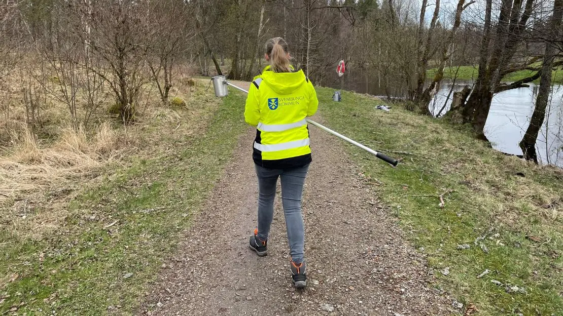 Person med kommunjacka går längs med Ätran och bär ett provtagningskit.