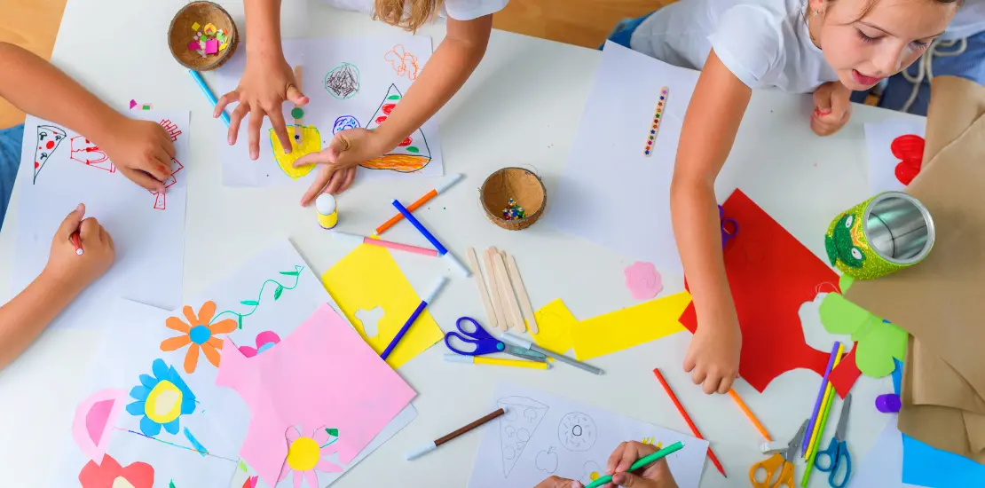 Barn som sitter vid ett bord och målar och klipper i papper.