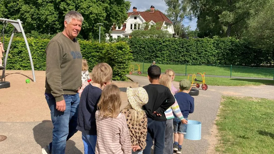 Förskoleklass står på rad bredvid en vuxen på lekplats.
