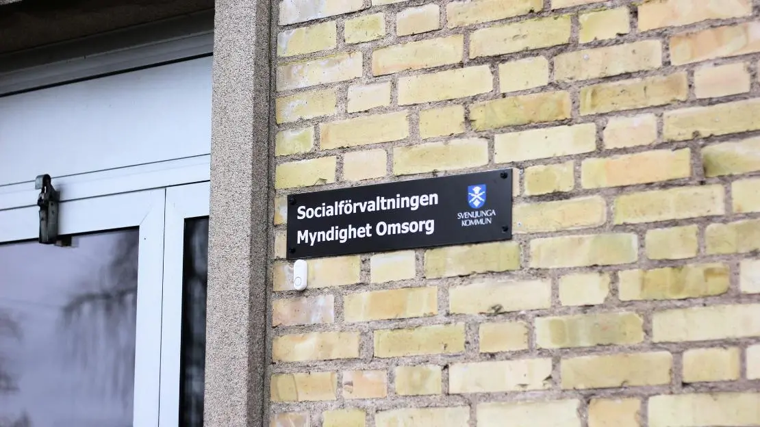 Skylt på gul tegelvägg med texten "Socialförvaltningen Myndighet Omsorg" och Svenljunga kommuns logga.