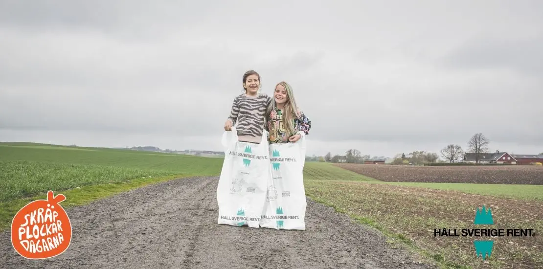 två personer står på en väg med varsin stor soppåse