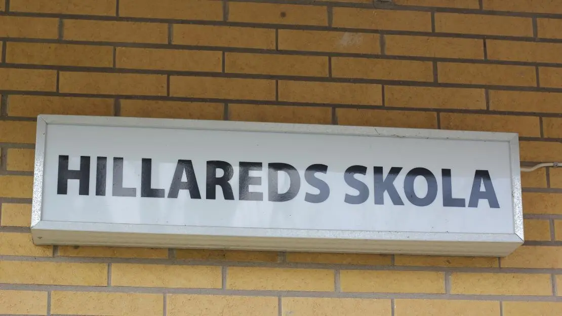 Skylt med texten Hillareds skola fäst på gul tegelvägg.