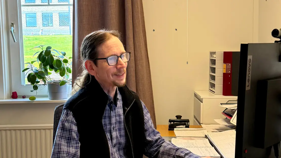 Ulrik sitter framför datorn och läser på skärmen. Bakom honom syns ett fönster.