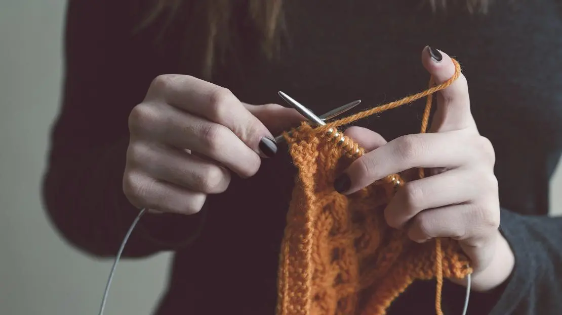 Person stickar med orange garn.