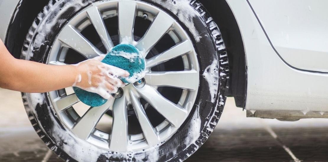 Person tvättar bildäck med såpa och tvättsvamp.