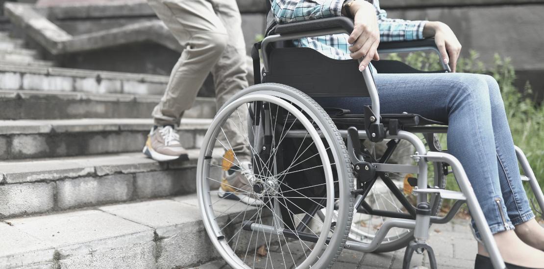 En person hjälper en annan att ta sig upp- eller nerför en trappa i rullstol. 