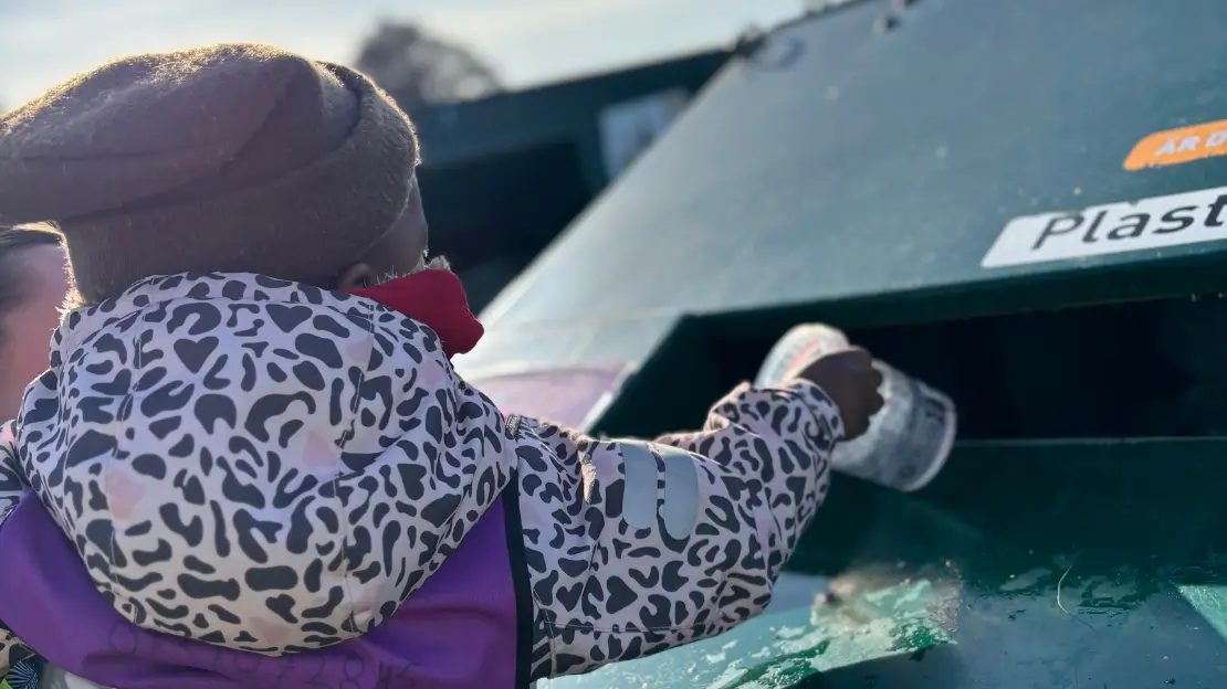 Ett barn sorterar en plastlåda i en sopcontainer för plastförpackningar. 