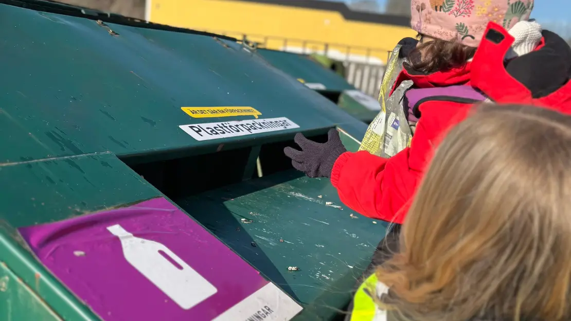 Ett barn lyfts upp för att sortera plastförpackningar.