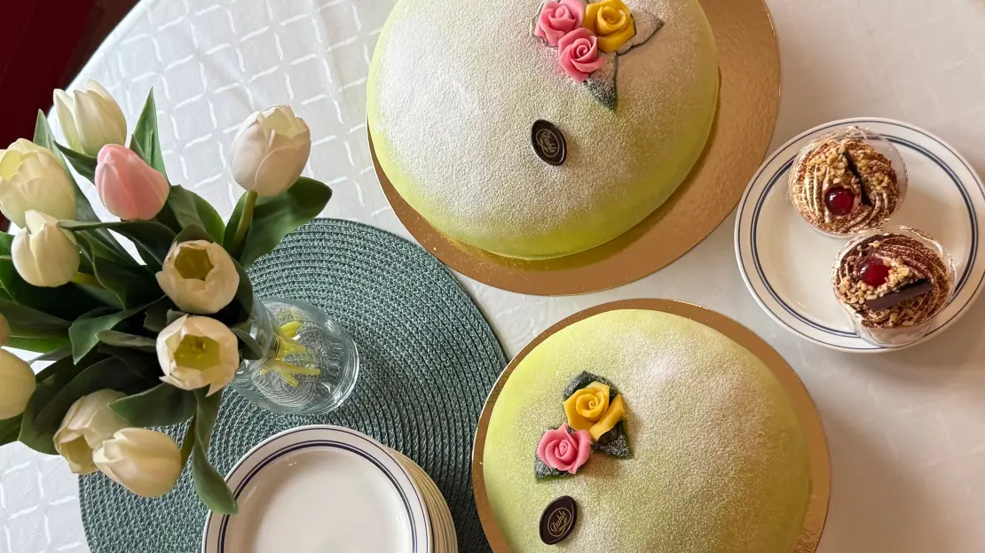 Två prinsesstårtor står på ett bord. På bordet står bukett med tulpaner, tallrikar och en tallrik med två bakelser på. 