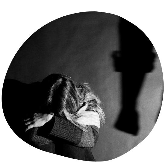 Svartvitt bild på kvinna som gömmer sitt ansikte mot sina knän och armar, på väggen bakom syns skuggan av en knytnäve.