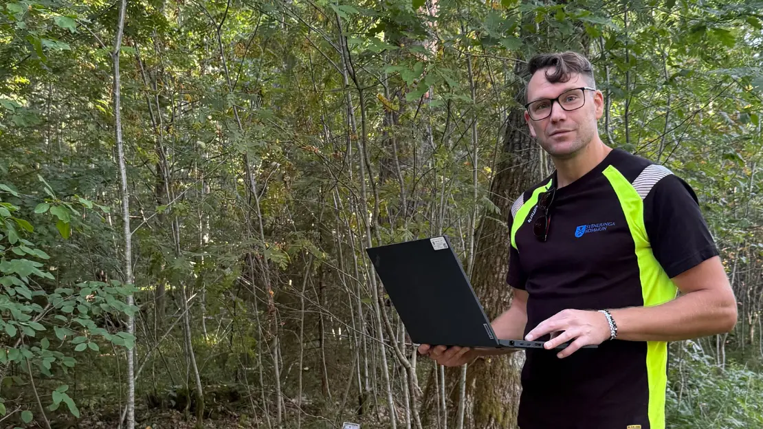 Christoffer Österling står i skogen med en laptop i handen.