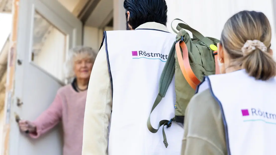 Två röstmottagare står i en trappa utanför en röstares hem. Röstaren har öppnat upp sin dörr och tar emot dem.