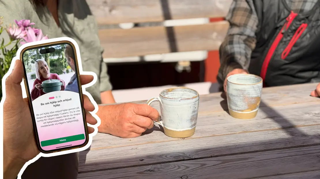 Två personer sitter och dricker kaffe. I förgrunden syns en hand med en mobil som visar Commuappen.