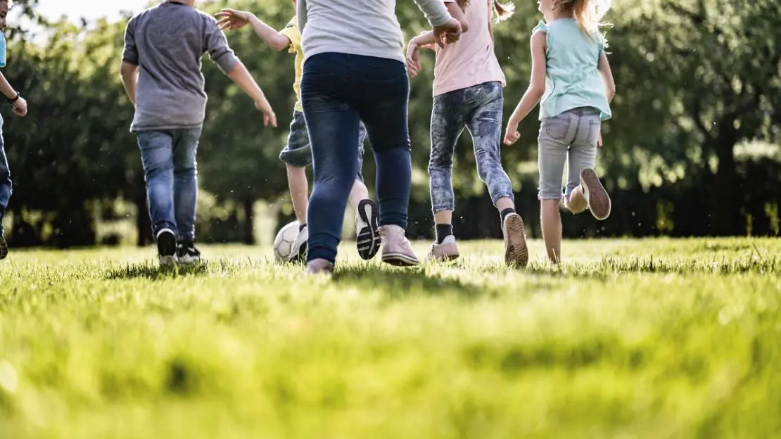 Barn springer på en grön äng.
