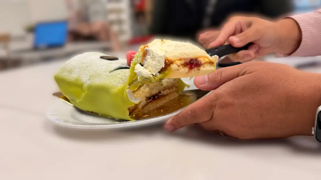 Någon skär en bit av en grön tårta med flera lager. Tårtan har en frosting och är placerad på en silverbricka.