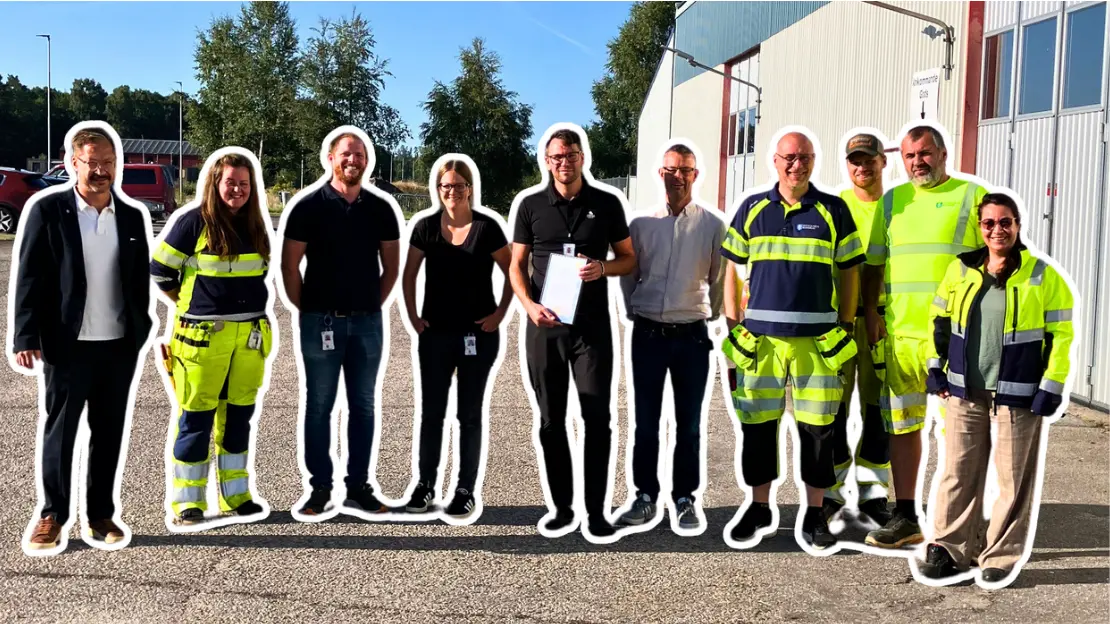 En grupp personer står utomhus, en person håller i en inramad diplom. Det är soligt och fint väder. se ser glada ut.