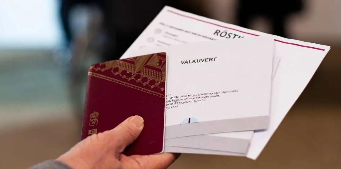 Person håller upp röstkort, valkuvert och pass.