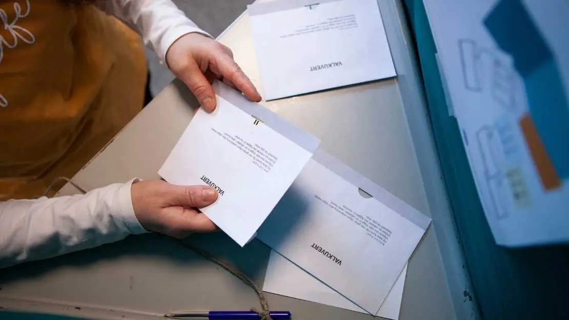 Person håller i ett valkuvert bakom en röstskärm.