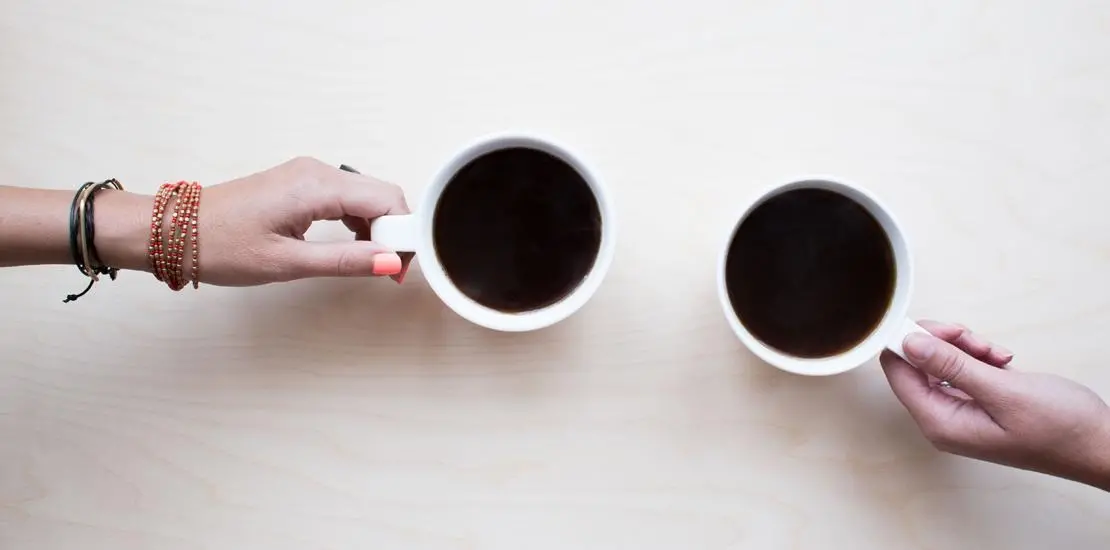 två olika händer som håller i kaffekoppar med kaffe i