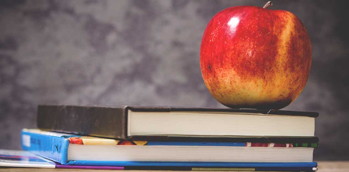 Två böcker som ligger på bordet med ett äpple som står uppe på 