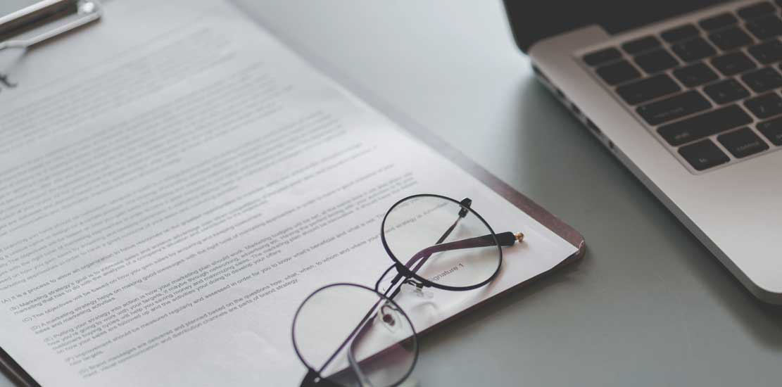 Glasögon ligger på ett paper bredvid en laptop.