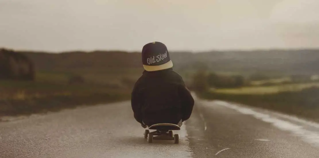 en liten kille som sitter på en skateboard som rullar ner för en väg