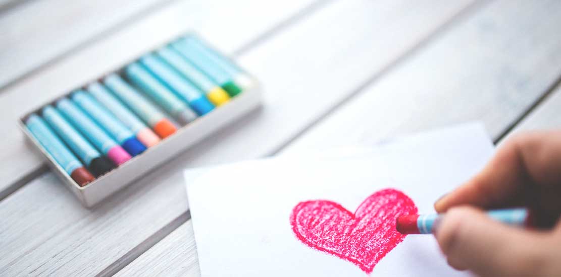 Någon som målar ett rött hjärta på ett papper med kritor