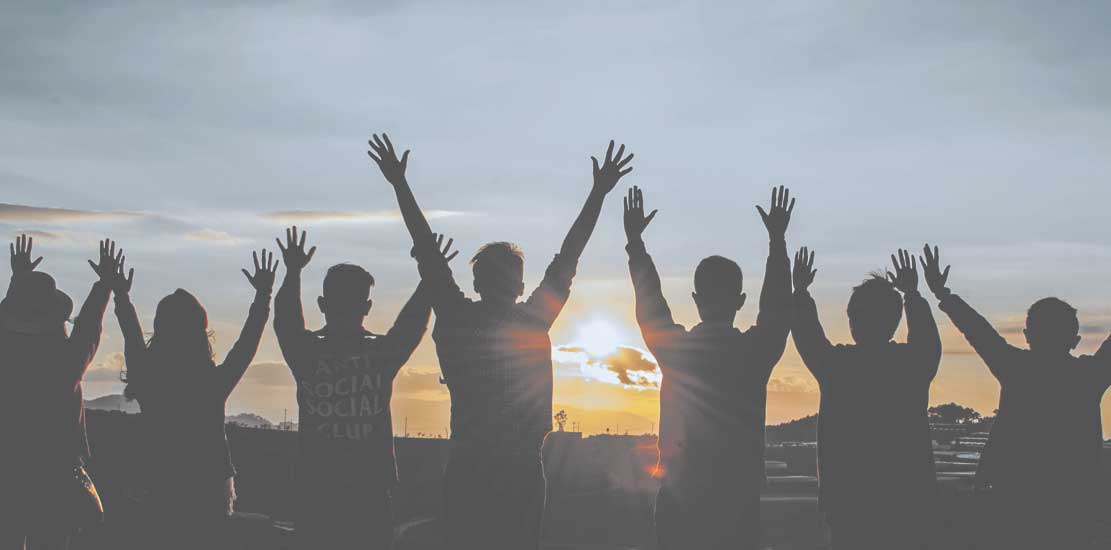 ungdomar håller sina händer upp mot himlen i en solnedgång