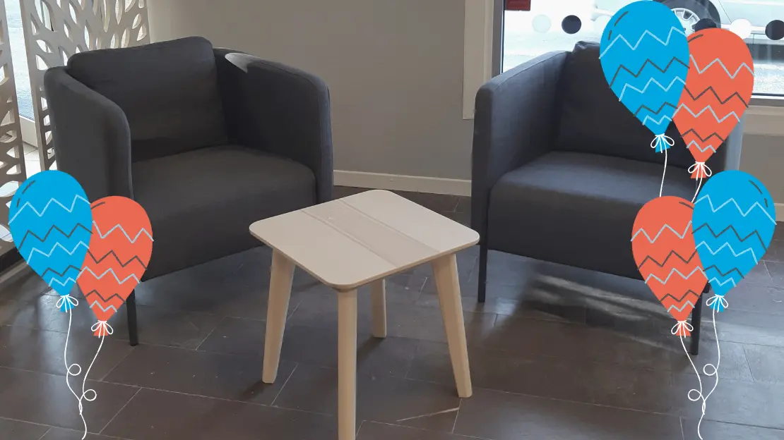 två gråa fåtöljer står varsin sida om ett litet bord inne i Aktivitetshus Hammarlind, tecknade ballonger framför