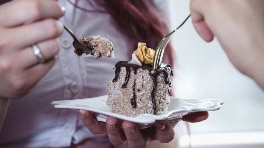 En person håller en tallrik med en tårtbit samtidigt som två personer tar med gaffeln från tårtbiten.