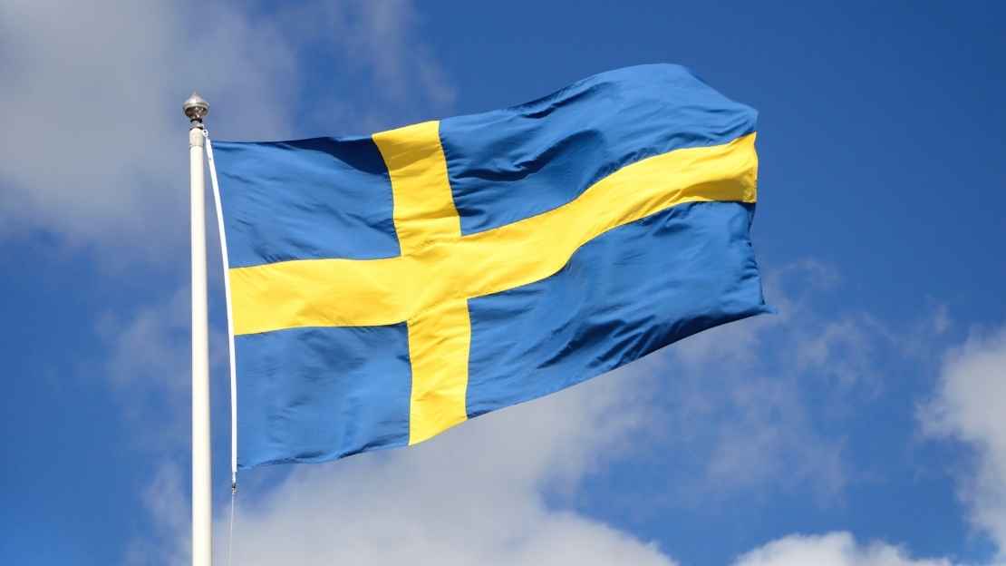Svensk flagga mot blå himmel med några få vita moln.
