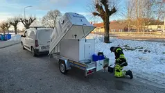Person i varselkläder tar vatten från en tank som står på ett släp bakom en vid transportbil.