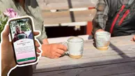 Två personer sitter och dricker kaffe. I förgrunden syns en hand med en mobil som visar Commuappen.
