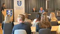Personer sitter i rader med ryggen vänd mot kameran, framför dem står någon vid en talarstol med Svenljunga kommuns vapen på samt bakom sig, bredvid sitter två personer.