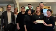 En grupp människor står med en tårta och ser glada ut.