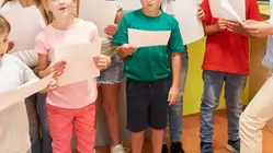 Flera barn står samlade i en grupp och håller noter i sina händer.