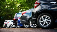 Bilar som står på parkering taget från sidan med gröna buskar i bakgrunden.