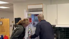 Två personer står och tittar in i ett kylskåp fullt med mat.