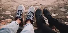 två personers fötter, den ena har kängor den andra gympaskor. 