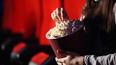 Person sitter i biograffåtölj och äter popcorn.