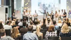 En publik bakifrån som tittar mot en scen där en grupp står och klappar händer och firar.