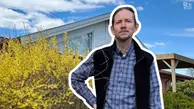 Ulrik står framför en buske med gula blommor. I bakgrunden syns en husfasad.