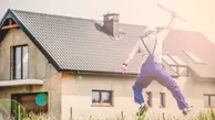 nybyggt hus, framför hoppar en byggarbetare med hjälm upp i luften och håller upp pappersrulle med ritningar