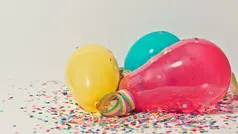 Tre färgglada ballonger ligger på golvet tillsammans med konfetti.