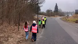 elever med färgglada reflexvästar går tillsammans två och två vid sidan av en väg.